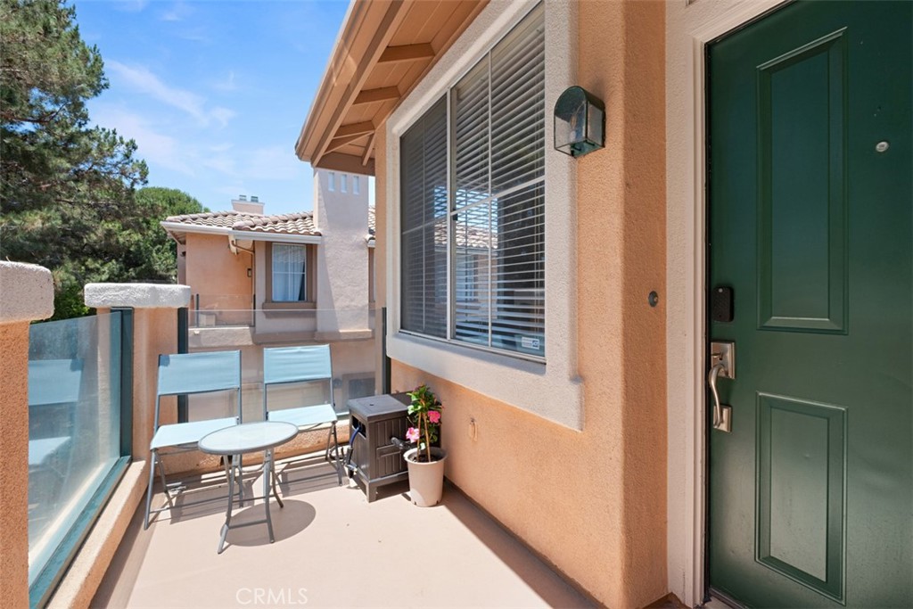 Balcony with glass railing, patio table and chairs, and a dark green entry door.