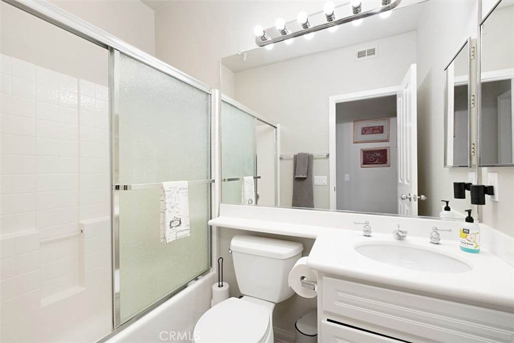 Bathroom with a white vanity, mirrored wall, and bathtub behind frosted glass shower doors.