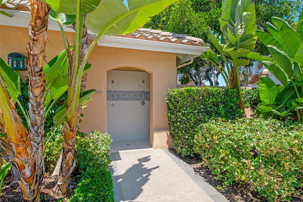 Outdoor shower entrance framed by banana plants and neatly trimmed hedges.