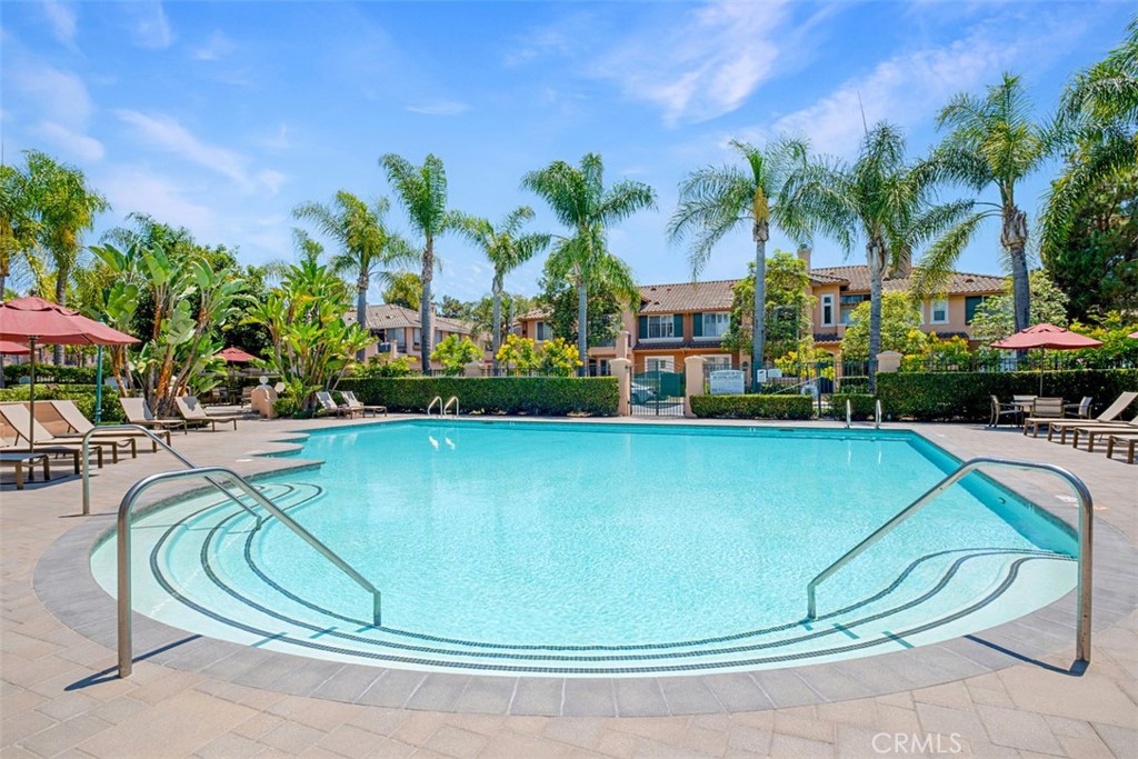 Community swimming pool with curved steps, palm trees, and lounge chairs beside two-story homes.