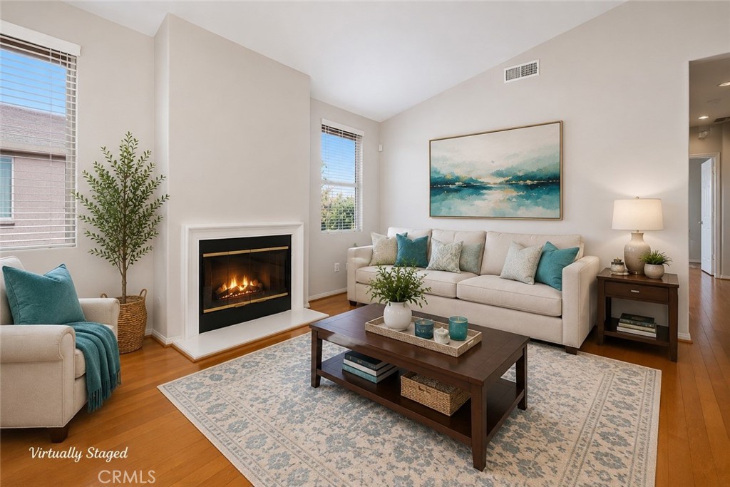 Living room with a lit fireplace, cream seating, teal accents, and hardwood floors.