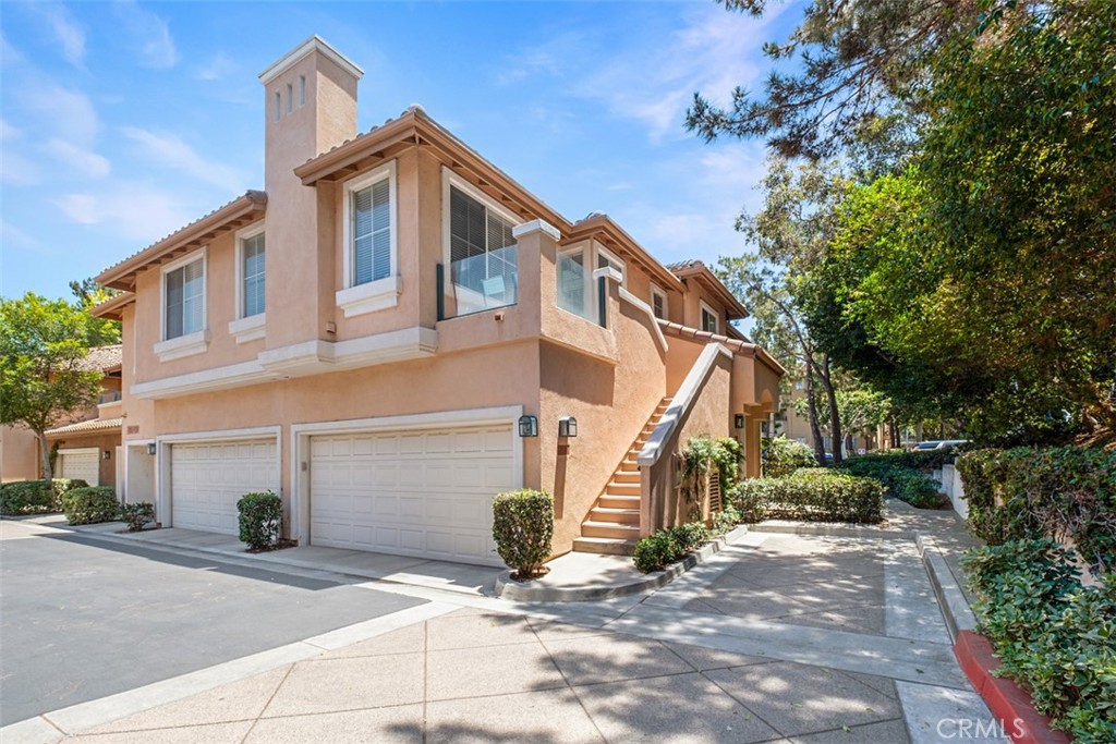 Two-story stucco home with two garage doors, an exterior staircase, and an upper-level balcony.