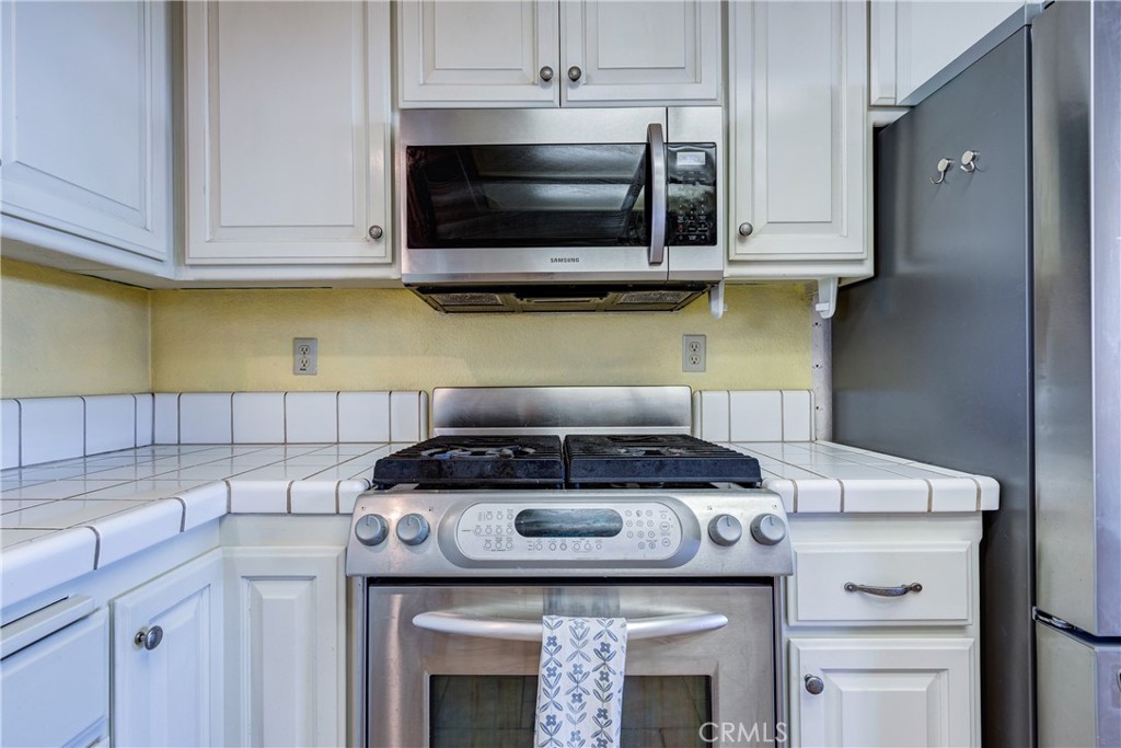 Kitchen with stainless steel range and microwave, white tile counters, and gray refrigerator.