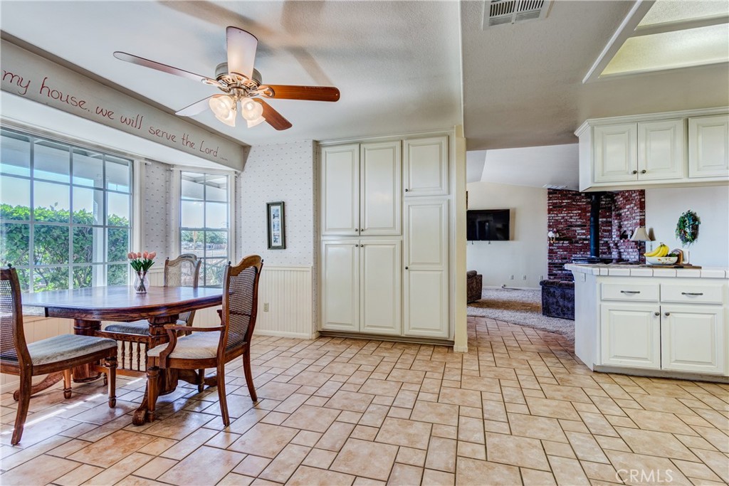 Kitchen and dining area with white built-in cabinets, tiled floors, and a wooden table beside large windows.