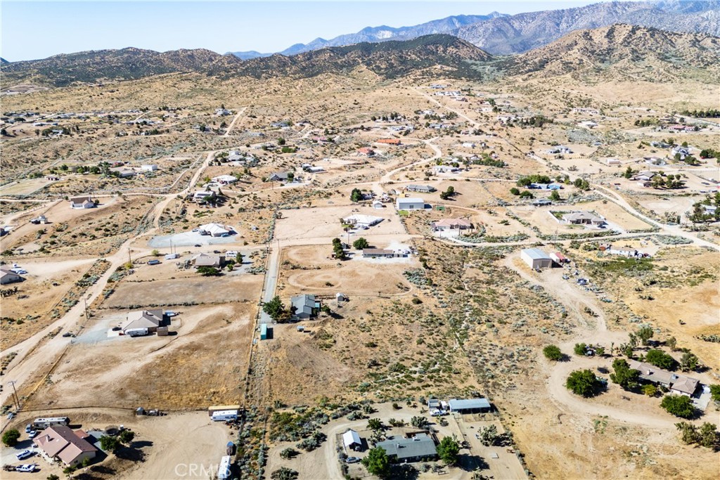 Aerial view of scattered rural homes, dirt roads, and mountains beyond dry foothills.