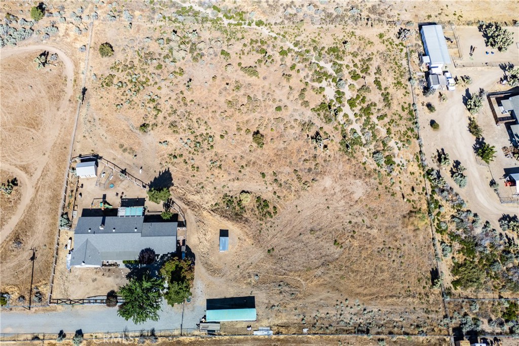 Aerial view of a rural property with a house, fenced yard, and open dry land.