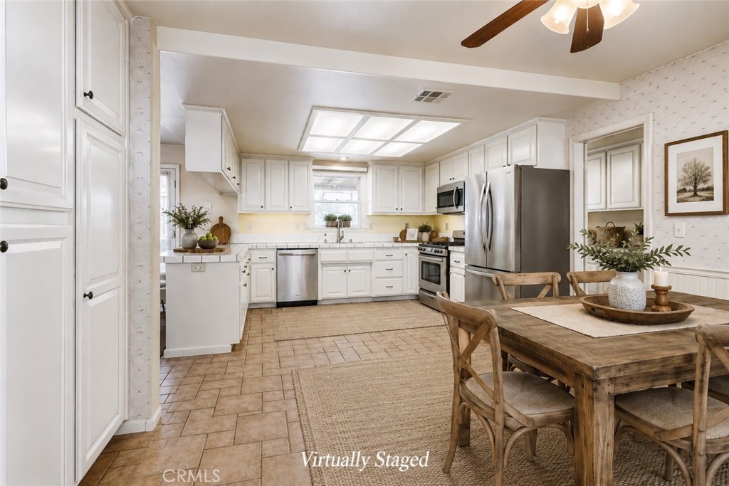 Kitchen with white cabinetry, stainless steel appliances, and a virtually staged wooden dining table.