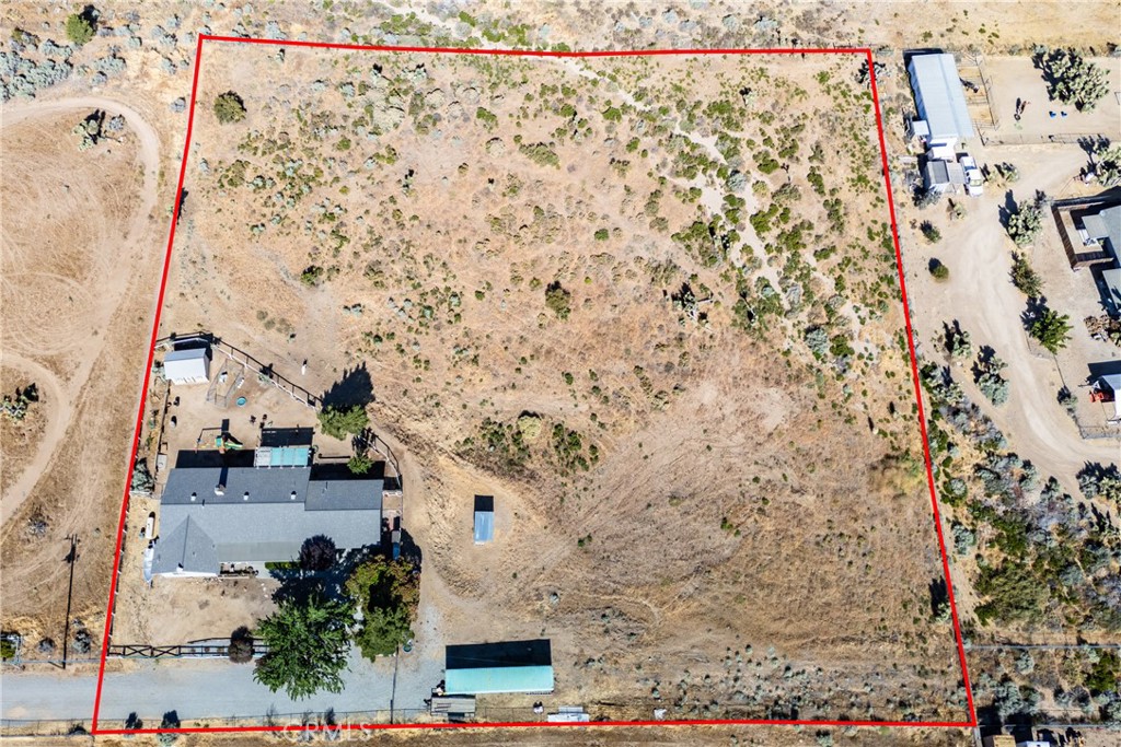 Aerial view of a dry, scrub-covered parcel outlined in red, with a house, fenced yard, and outbuildings.