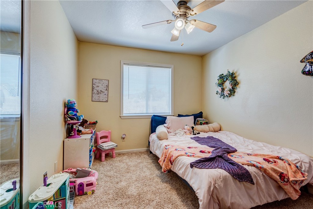 Bedroom with pink bedding, colorful blankets, toys, and a ceiling fan.