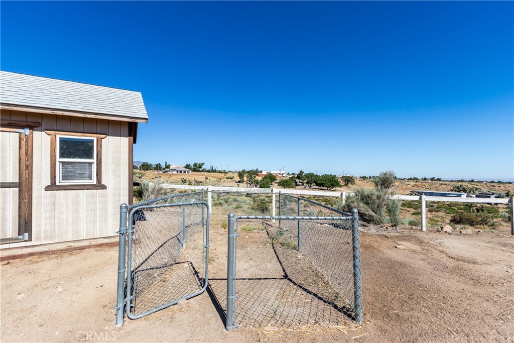 Rural property with a wood-sided outbuilding, chain-link gate, and dry scrubland.