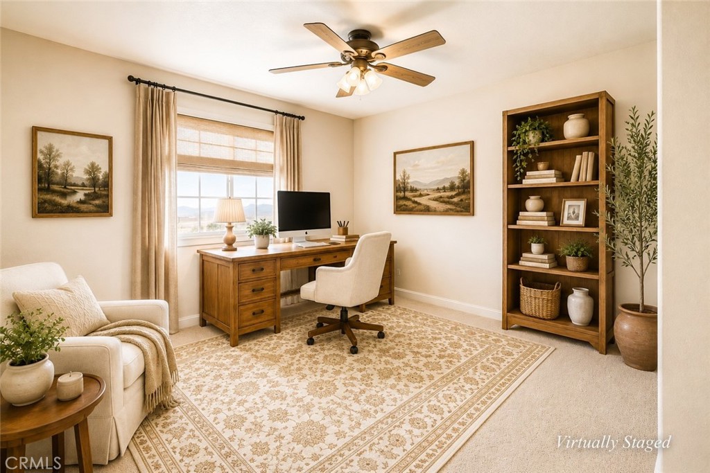 Home office with a wooden desk, tall bookcase, cream chair, and patterned rug.