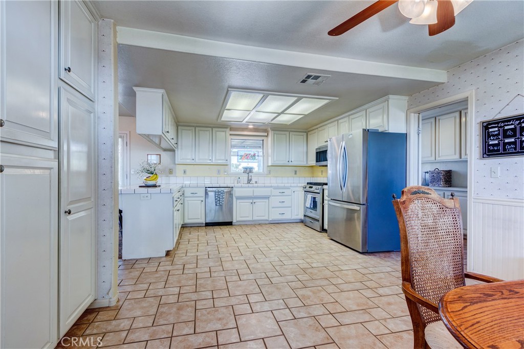 Kitchen with white cabinetry, stainless steel appliances, and tan tile flooring.