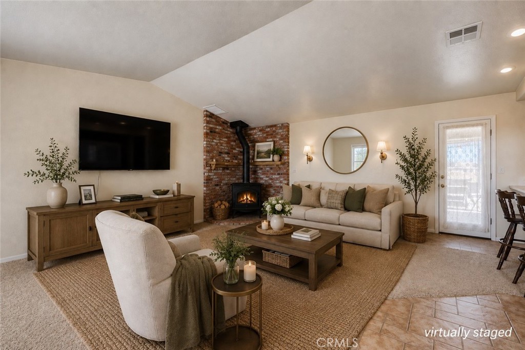 Staged living room with brick fireplace, neutral sofa, wall-mounted television, and woven rug.