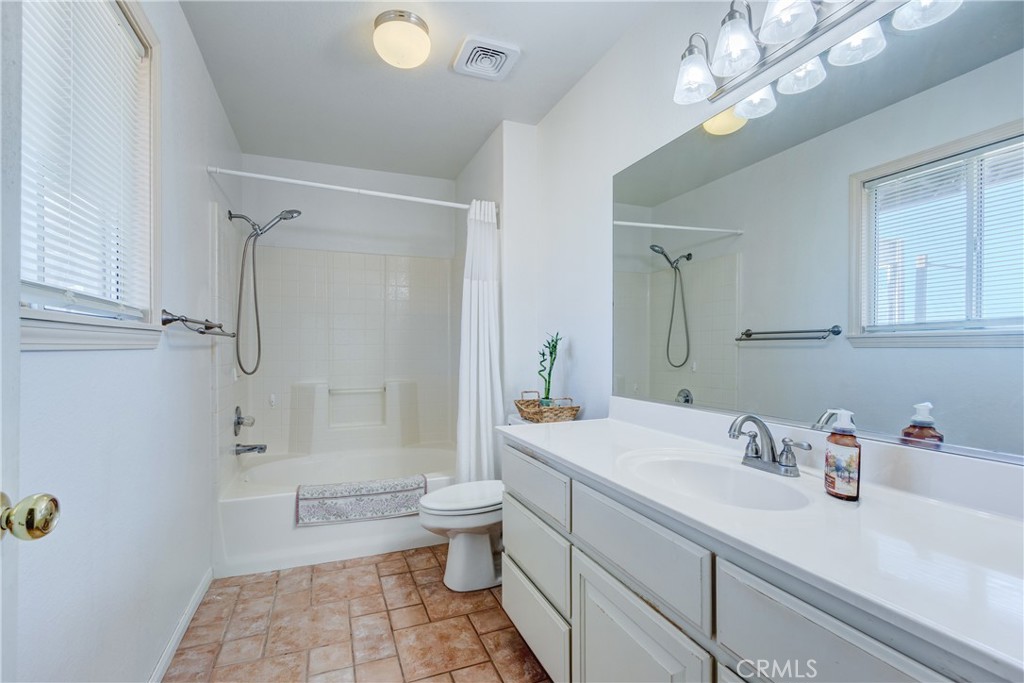 Bathroom with a curtained tub and shower, toilet, and long white vanity with a large mirror.