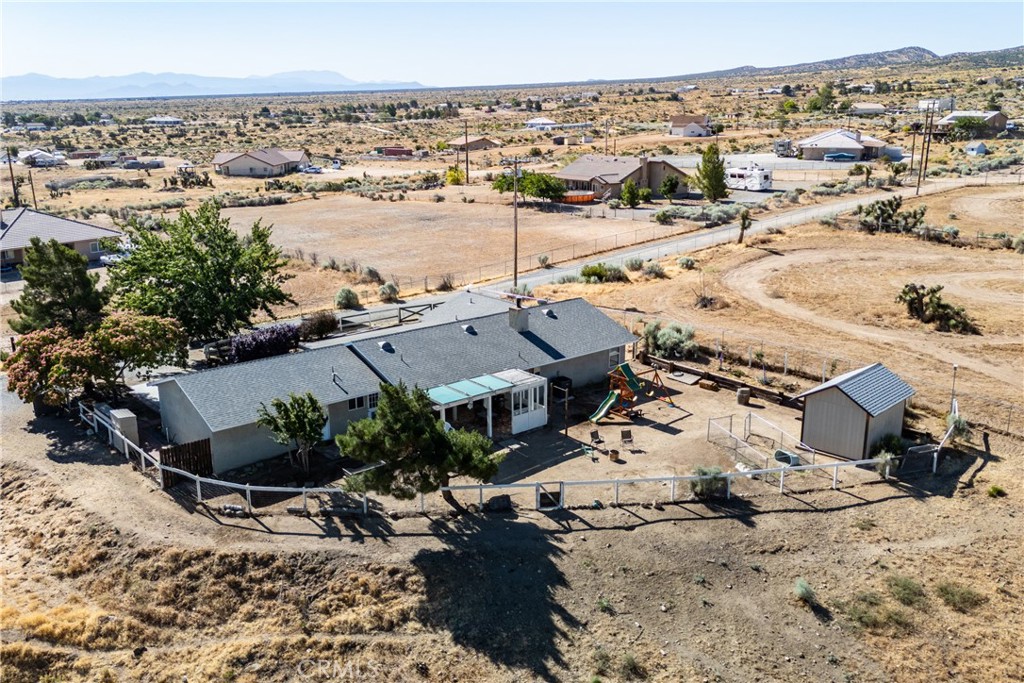 Aerial view of a fenced rural home with a backyard swing set and distant mountains.