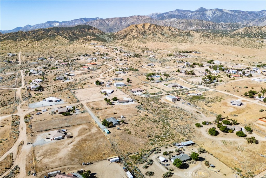 Aerial view of scattered homes and dry lots with rugged mountains in the distance.