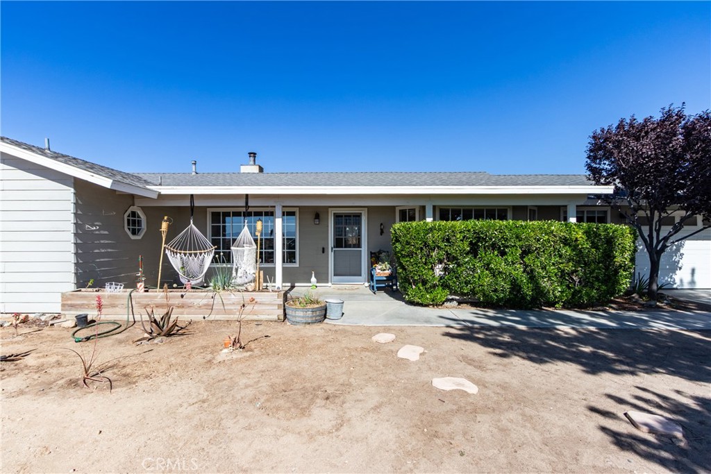 Single-story home with a covered patio, hanging hammock chairs, and a large trimmed hedge.