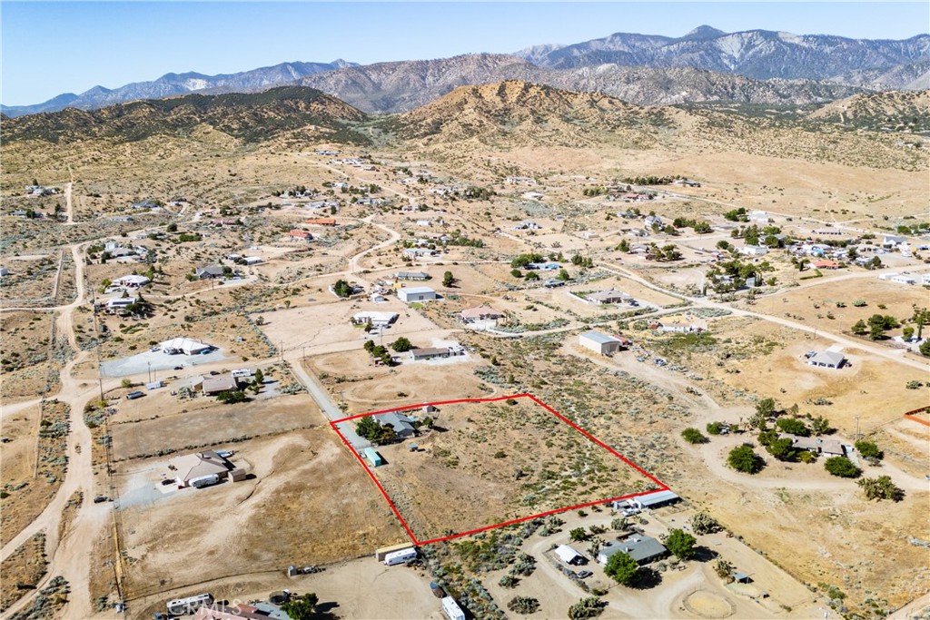 Aerial view of a mostly undeveloped parcel outlined in red, with mountain ranges beyond.
