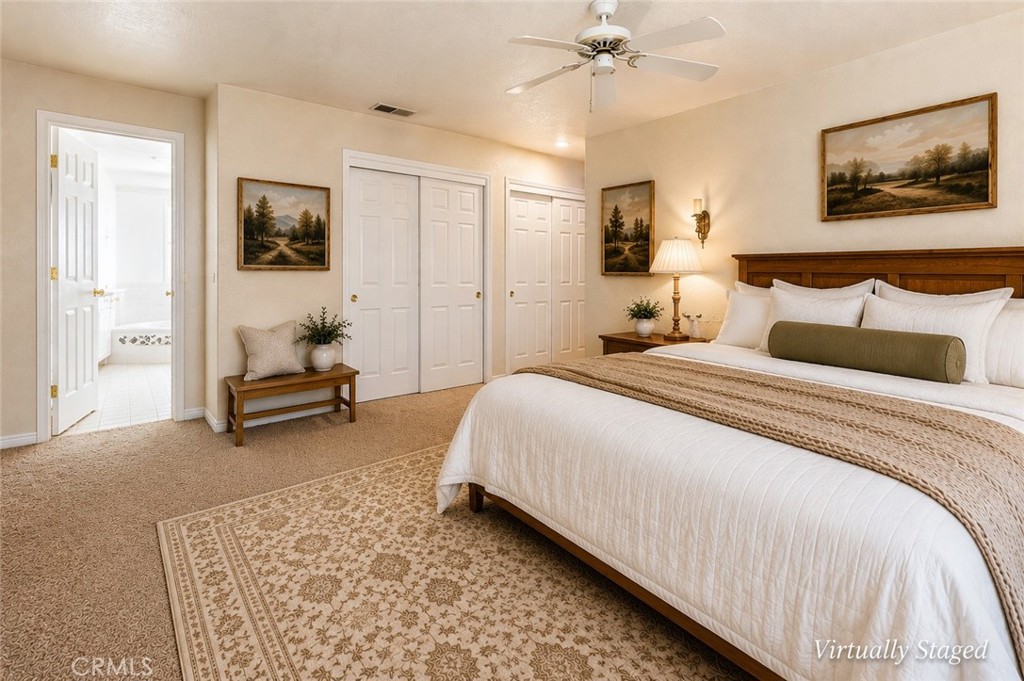 Virtually staged bedroom with a large bed, ceiling fan, patterned rug, and adjoining bathroom.