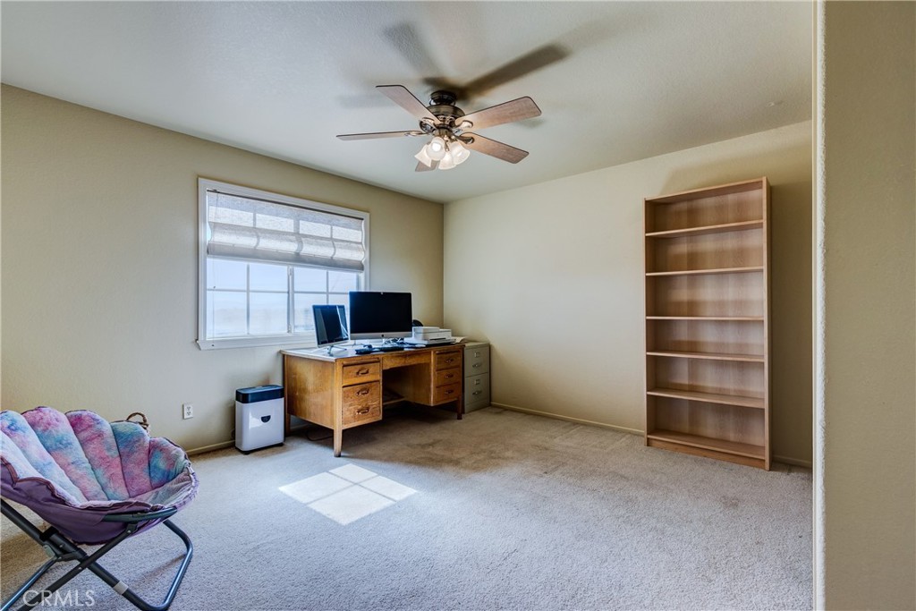 Carpeted home office with a wooden desk beneath the window and a tall bookcase.