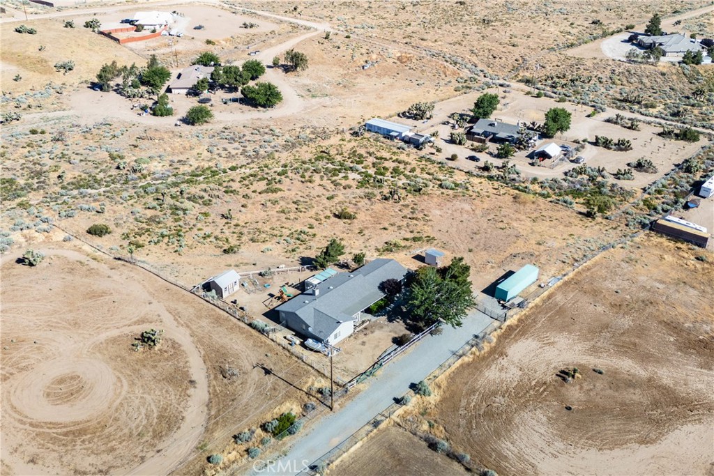 Aerial view of a fenced rural home with outbuildings and dry open acreage.
