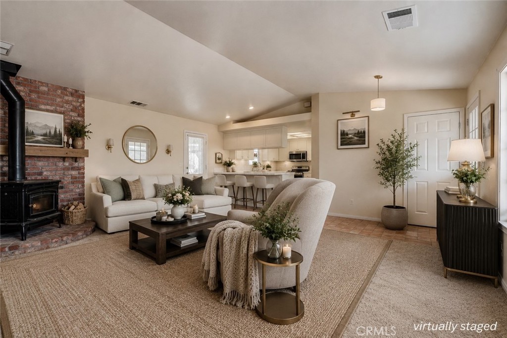 Virtually staged living room with brick fireplace, seating area, and open kitchen.