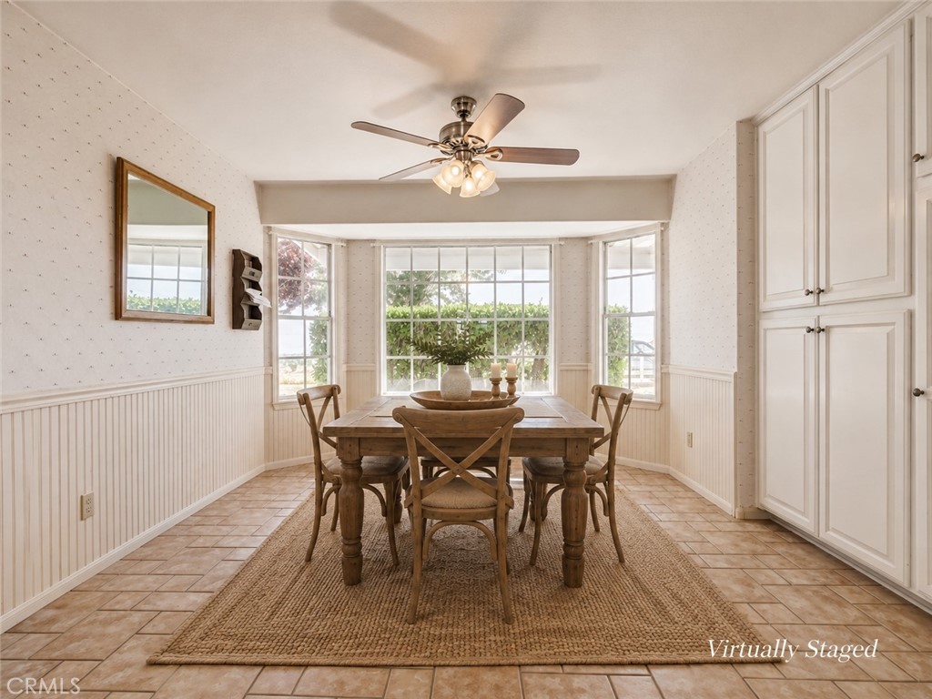 Dining room with a wooden table, bay windows overlooking greenery, and white built-in cabinets.
