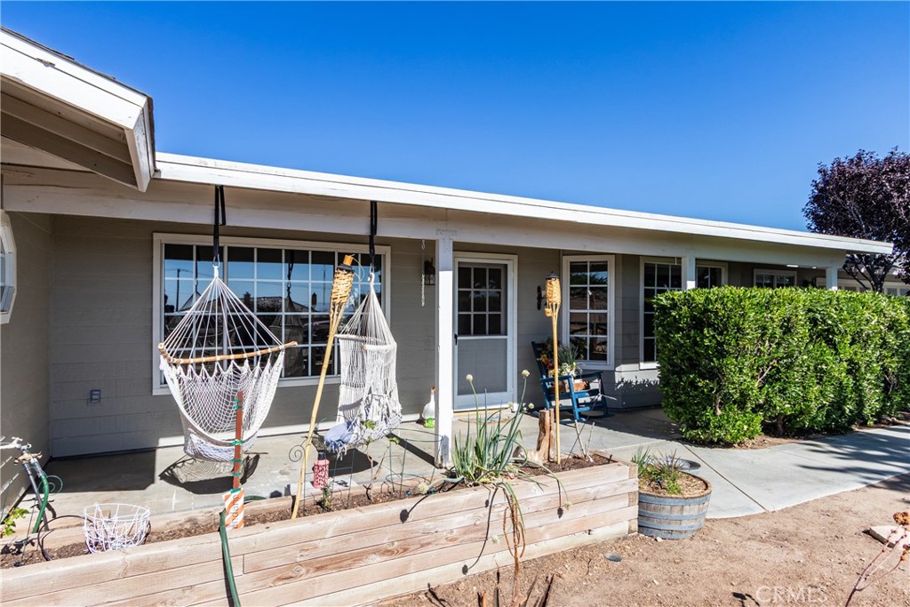 Single-story gray house with a covered patio, hammock chairs, and a raised wooden planter bed.