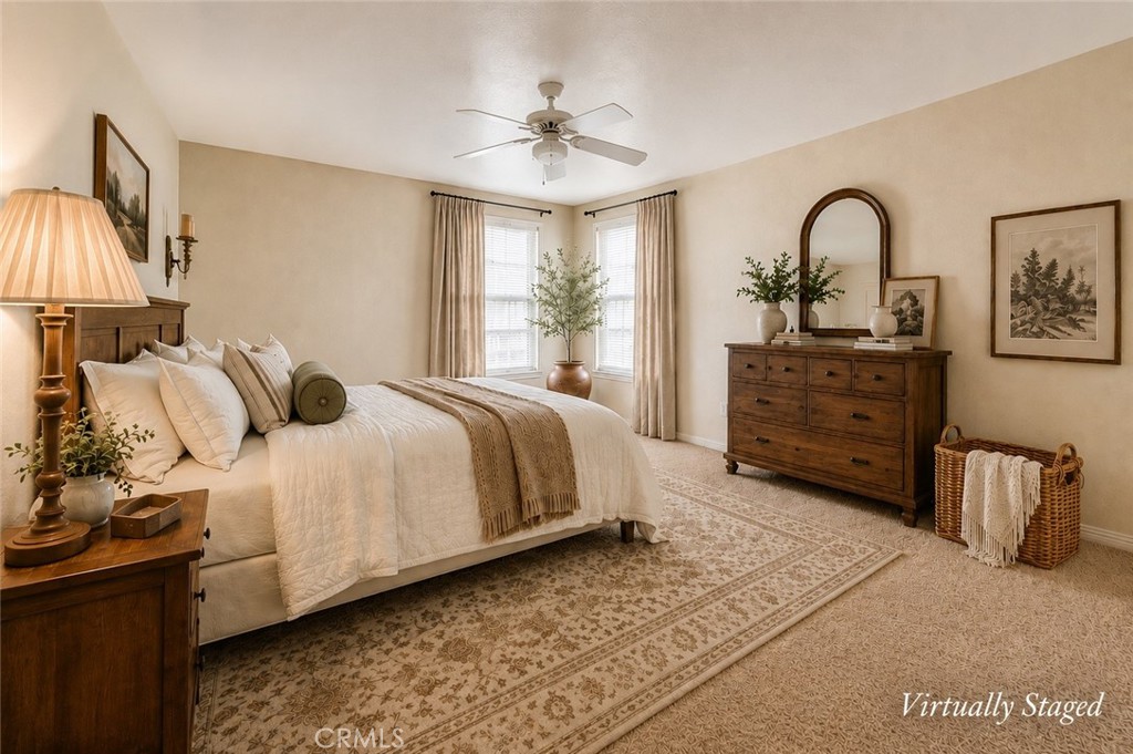 Bedroom with a large bed, patterned rug, wooden dresser, and two curtained windows.