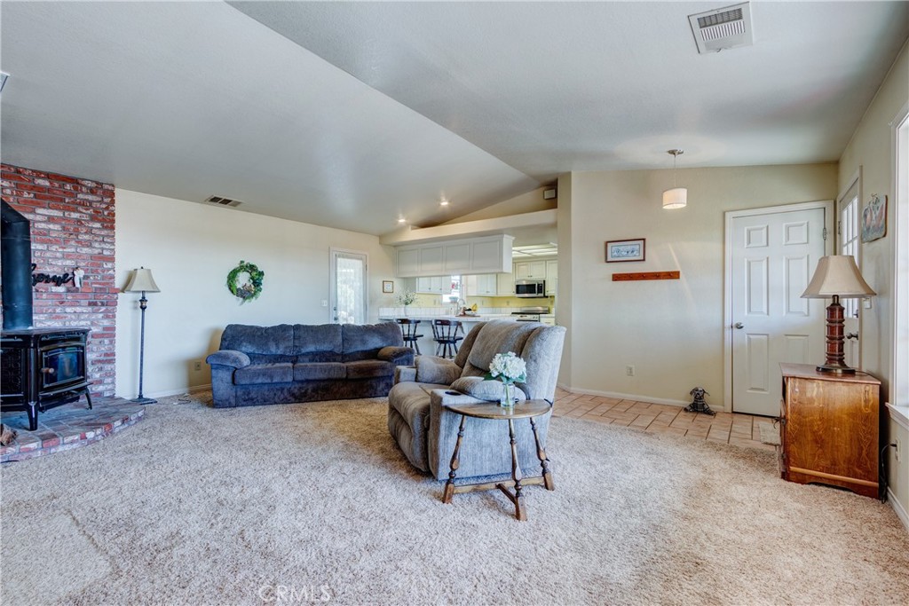 Living room with vaulted ceiling, blue seating, beige carpet, and a brick fireplace with a wood stove.