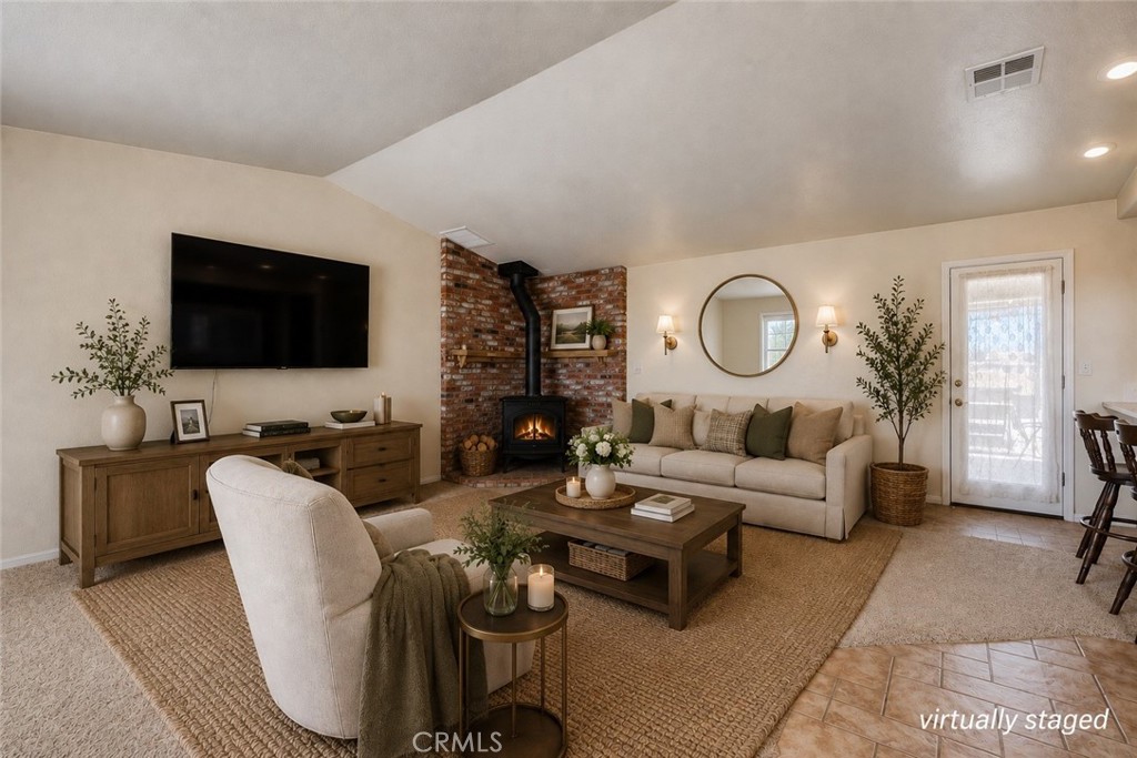 Virtually staged living room with a brick fireplace, lit wood stove, beige seating, and woven rug.