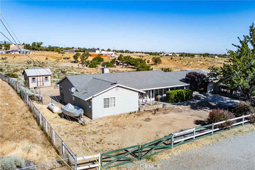Aerial view of a single-story home with a gray roof, fenced yard, and detached outbuilding.