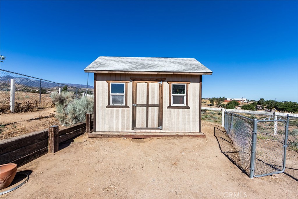 Detached shed with two windows and a central door in a fenced dirt yard.
