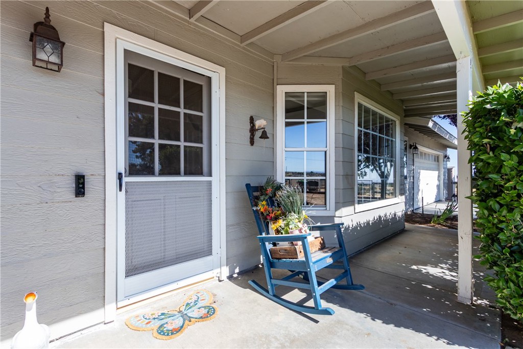 Covered home porch with a white screen door, blue rocking chair, flowers, and butterfly doormat.