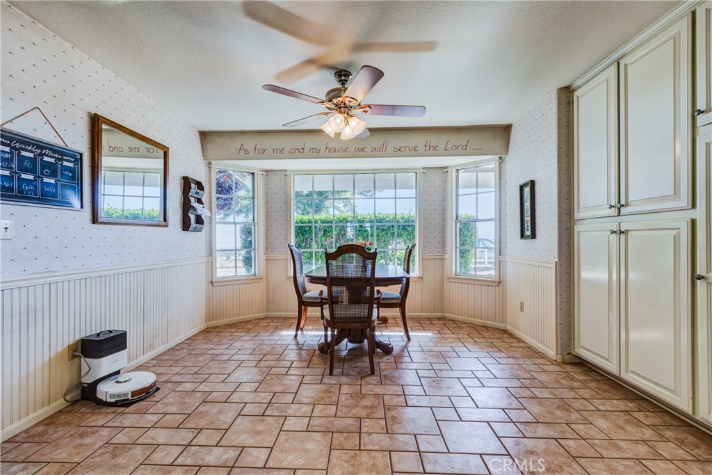Dining area with a round wooden table, large windows, cream built-in cabinets, and terracotta-colored tile flooring.