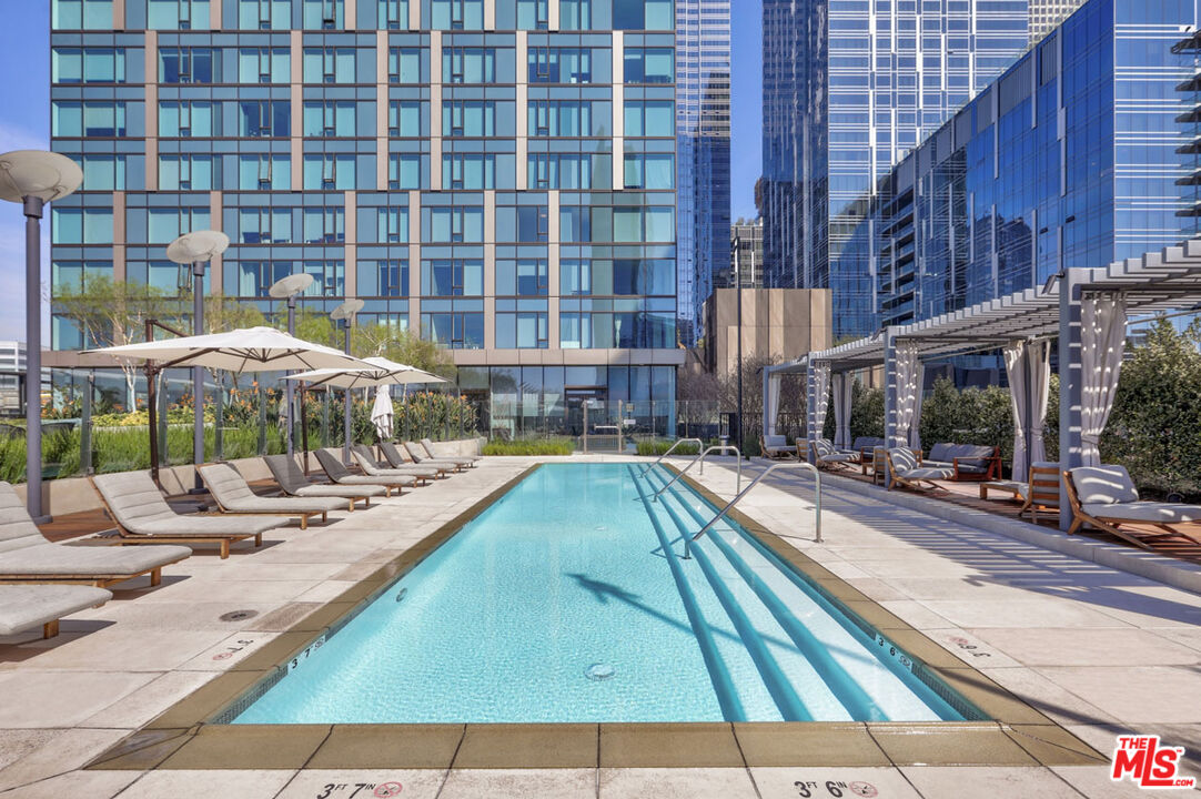 Outdoor pool with lounge chairs and umbrellas between modern high-rise buildings.