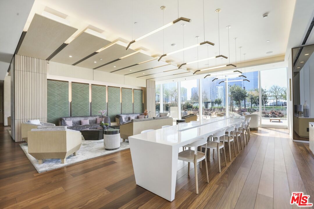 Residential building lounge with a long dining table, seating area, and floor-to-ceiling windows.