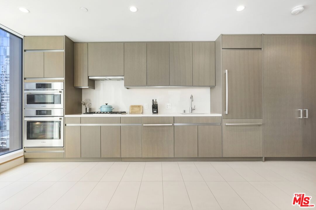 Modern kitchen with light wood cabinetry, built-in double ovens, and a window overlooking city buildings.