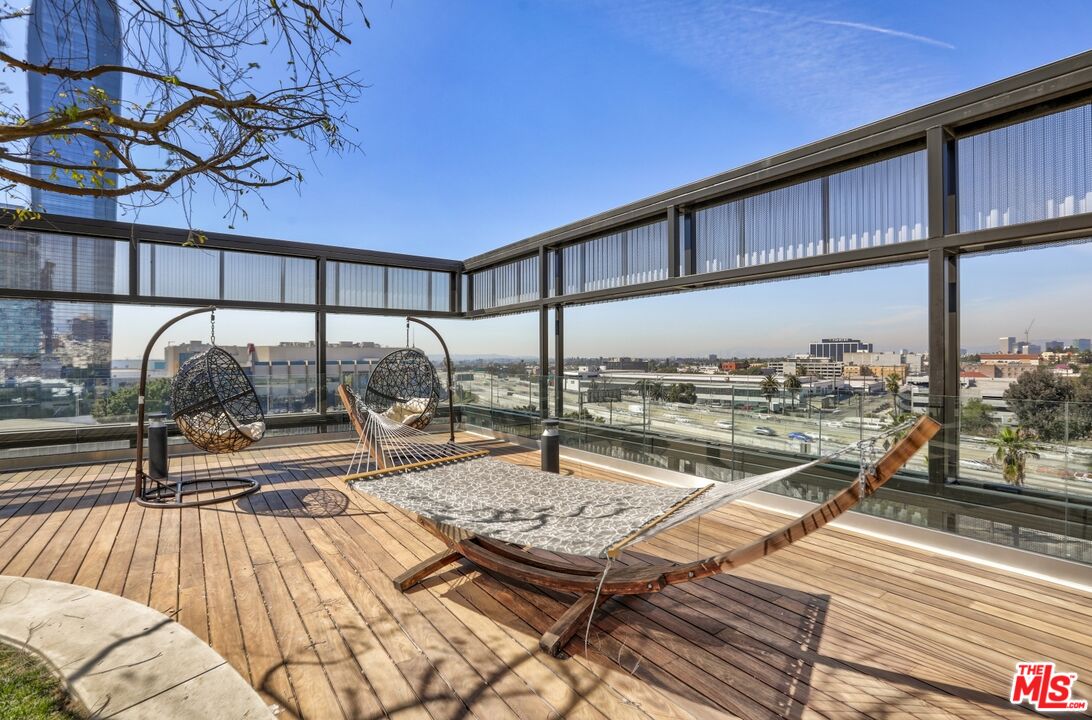 Rooftop deck with hanging chairs and a hammock overlooking city buildings.