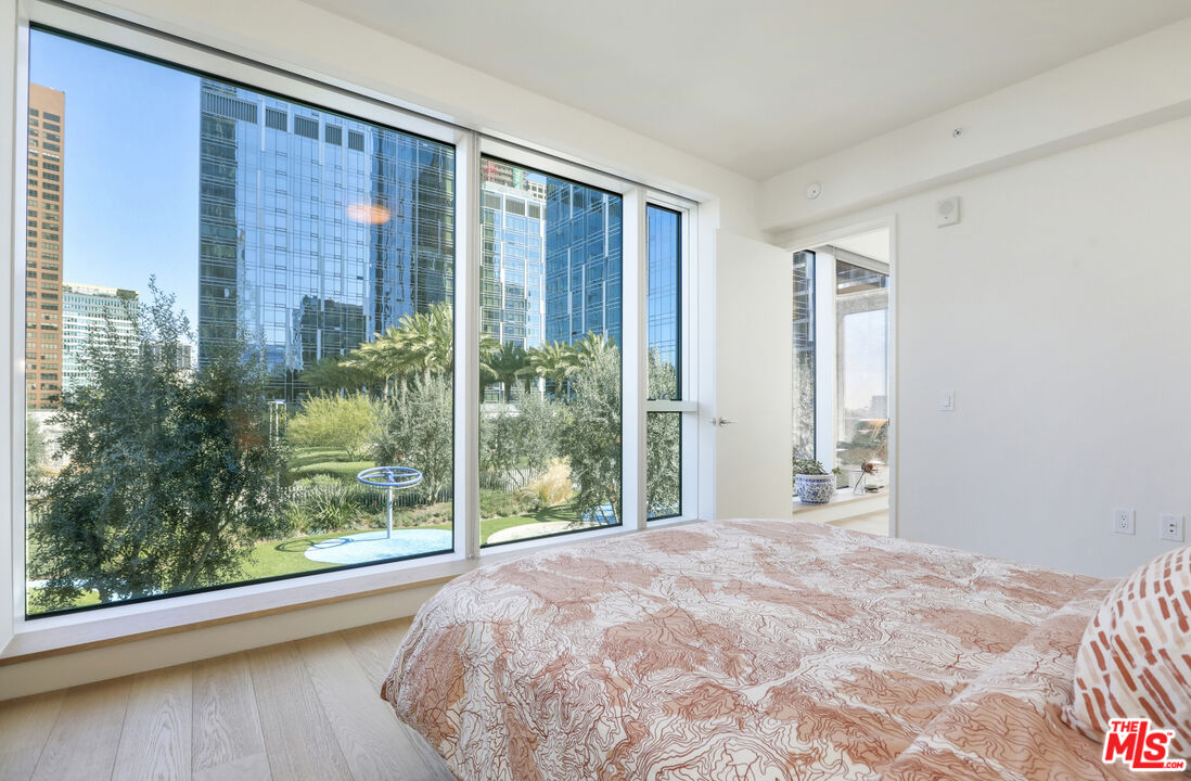 Bedroom with floor-to-ceiling windows overlooking landscaped grounds and downtown high-rises.