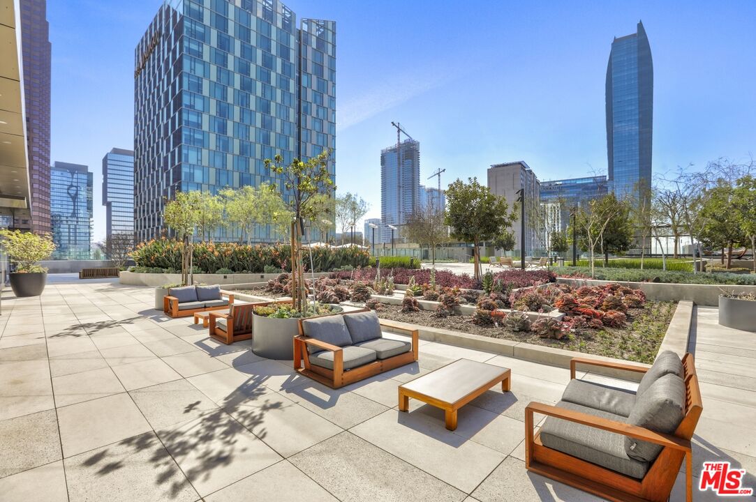Furnished terrace with landscaped garden beds and lounge seating, overlooking downtown high-rises.