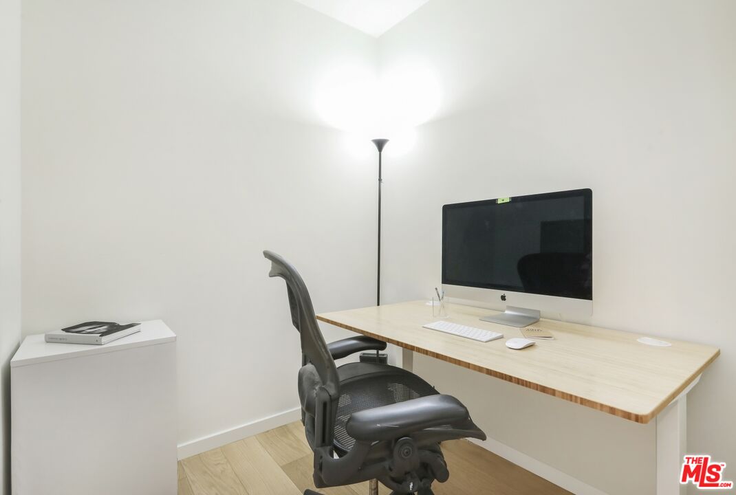 Home office with a light wood desk, desktop computer, and black ergonomic chair.