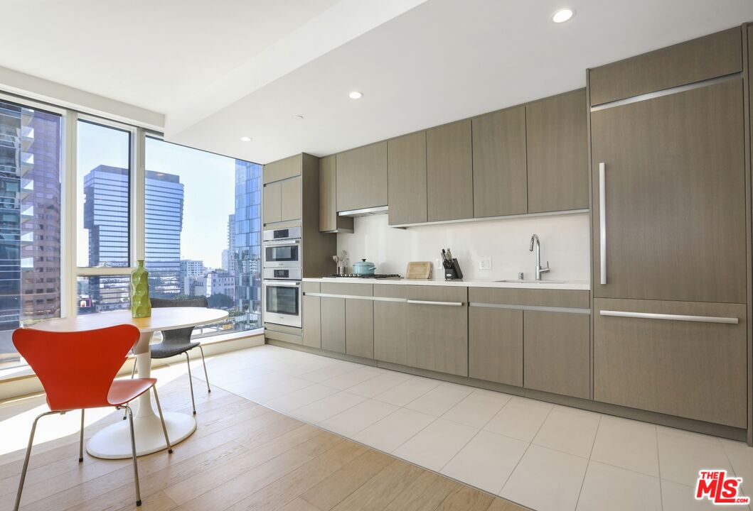 Modern condo kitchen with gray cabinetry and built-in ovens, plus downtown views through floor-to-ceiling windows.