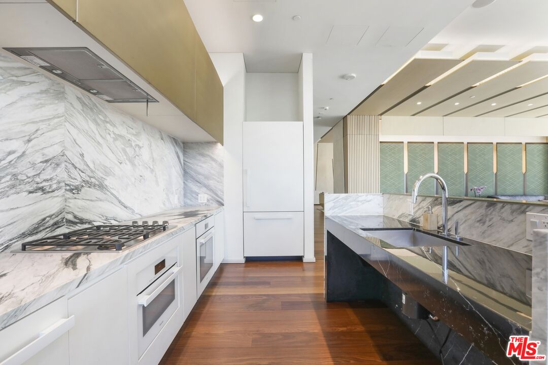 Modern kitchen with veined marble counters, a black island with double sink, and white cabinetry.