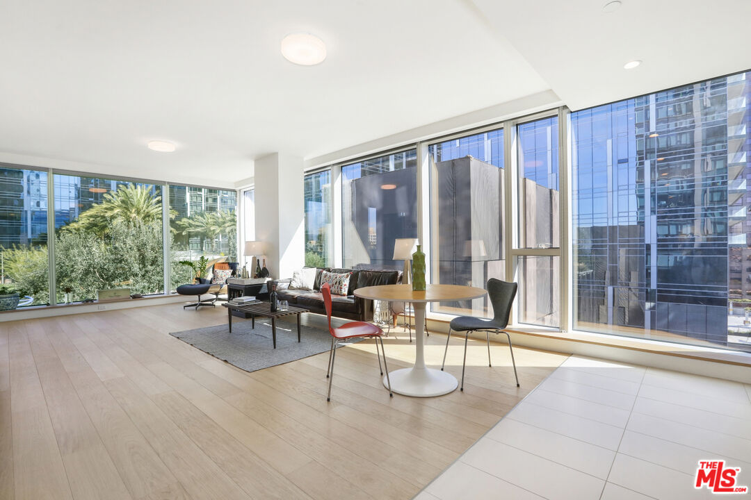 Furnished living and dining area with floor-to-ceiling windows overlooking nearby high-rises and trees.