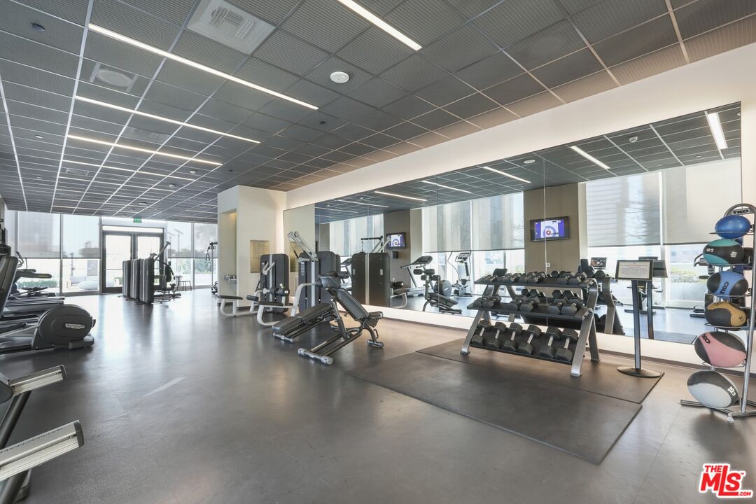 Residential fitness center with mirrored walls, dumbbell racks, and exercise machines.