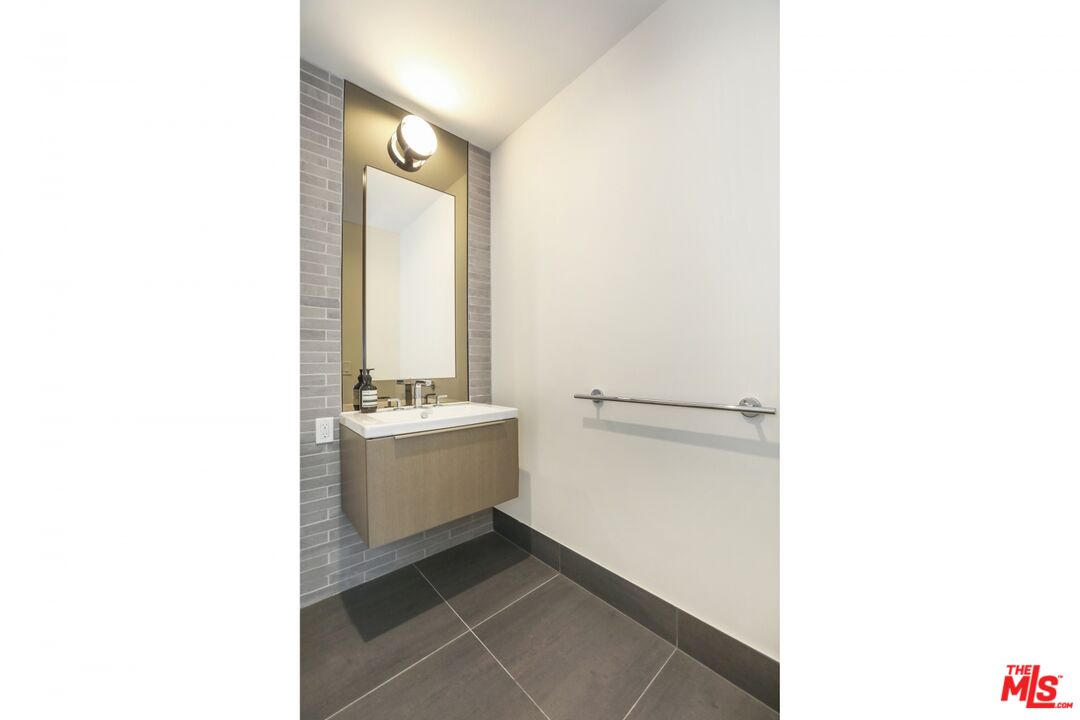 Modern bathroom vanity with a floating wood-tone cabinet, gray tile wall, and round mirror light.