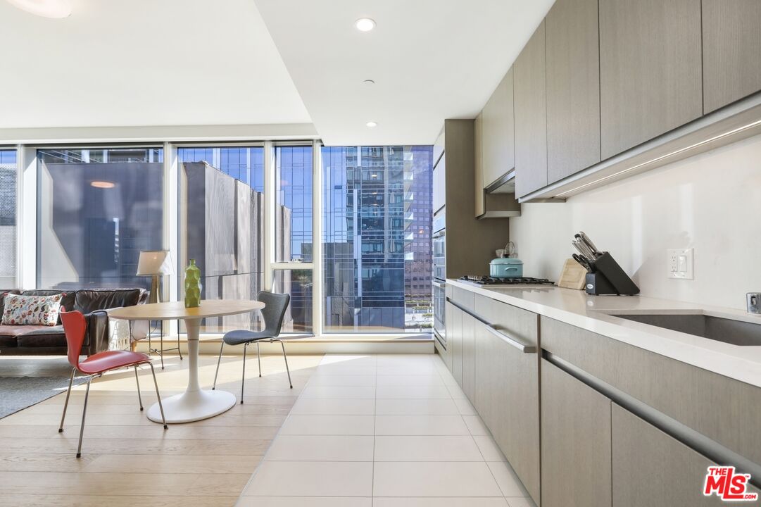Modern condo kitchen with gray cabinets, a dining area, and floor-to-ceiling windows overlooking high-rises.