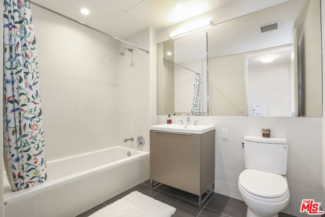 Bathroom with a white bathtub, patterned shower curtain, wood-tone vanity, and large mirrored cabinet.