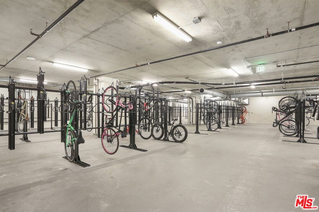 Bicycle storage room with rows of racks and bicycles beneath a concrete ceiling.